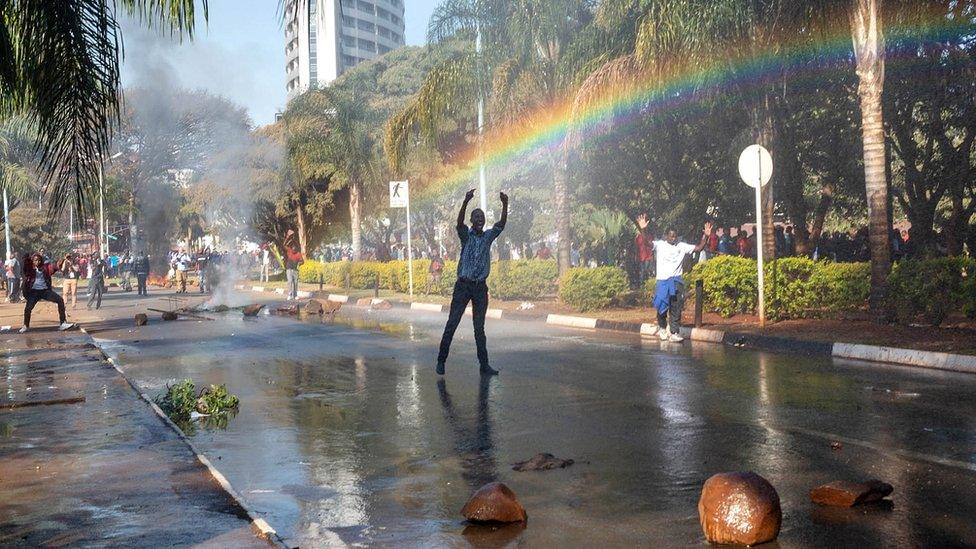 A protester gestures toward police water cannon outside the gates of the Zimbabwe Electoral Commission (ZEC) during a protest against polling results in Harare, Zimbabwe, 1 August 2018