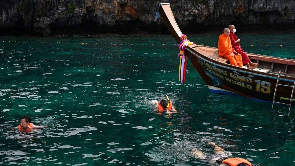 This picture taken on November 26, 2021 shows Buddhist monks resting in a longtail boat as tourists snorkel in Maya Bay on Thailand's Phi Phi Leh island