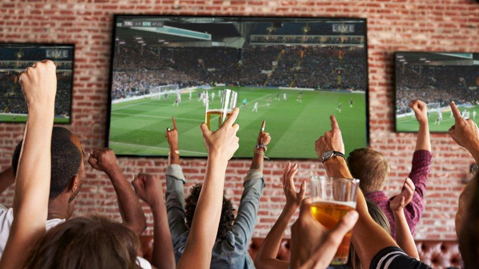 Rear view of people in a sports bar watching football on screens