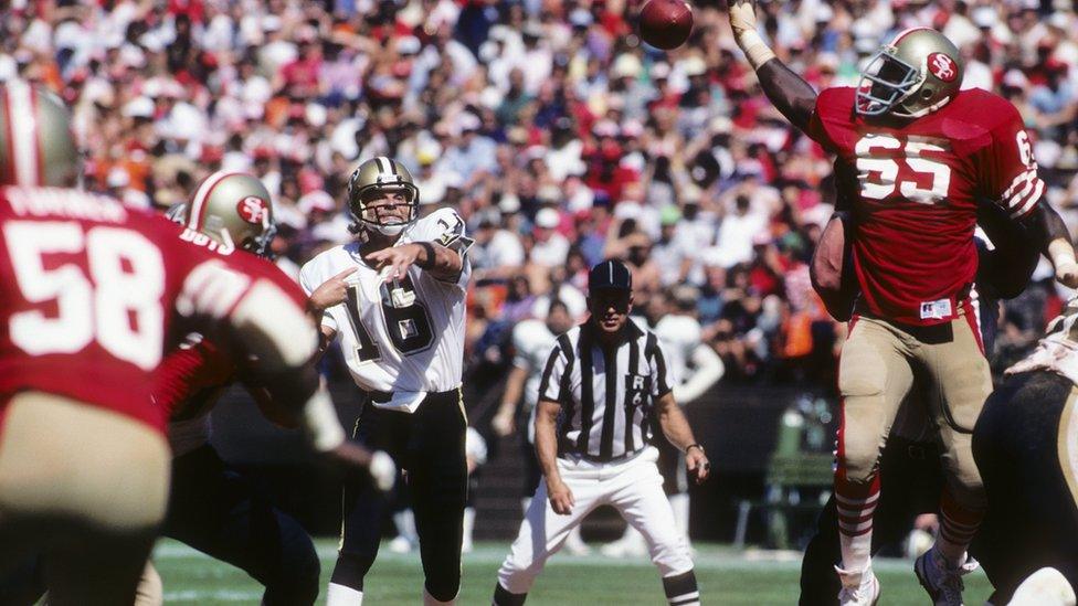 Defensive end Lawrence Pillers #65 of the San Francisco 49ers attempts to bat down a pass thrown by quarterback Ken Stabler #16 of the New Orleans Saints as NFL referee Tom Dooley #6 watches the action during a game at Candlestick Park on September 16, 1984 in San Francisco, California.