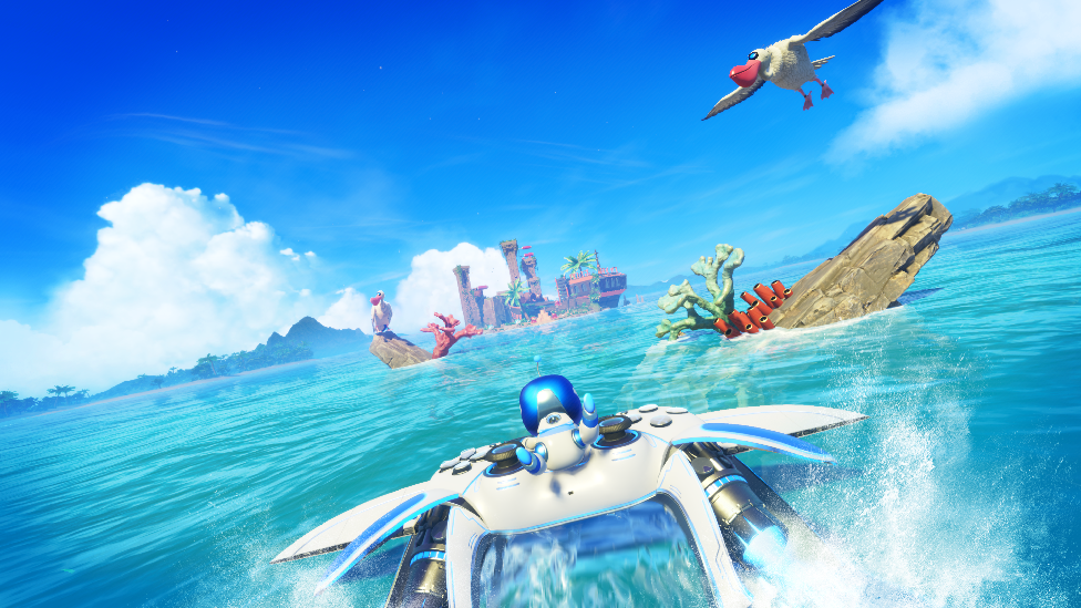 Screenshot shows Astro Bot gripping onto an oversized PS5 controller equipped with rockets as it skims across the surface of a perfect blue tropical sea towards an island.