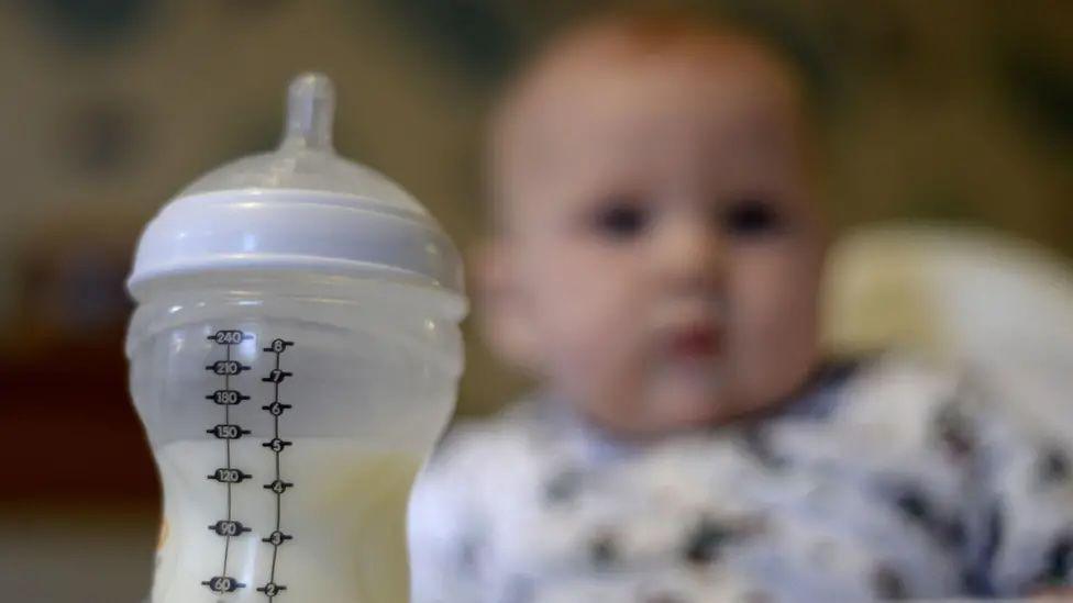A baby stares at a teeted bottle containing milk.
