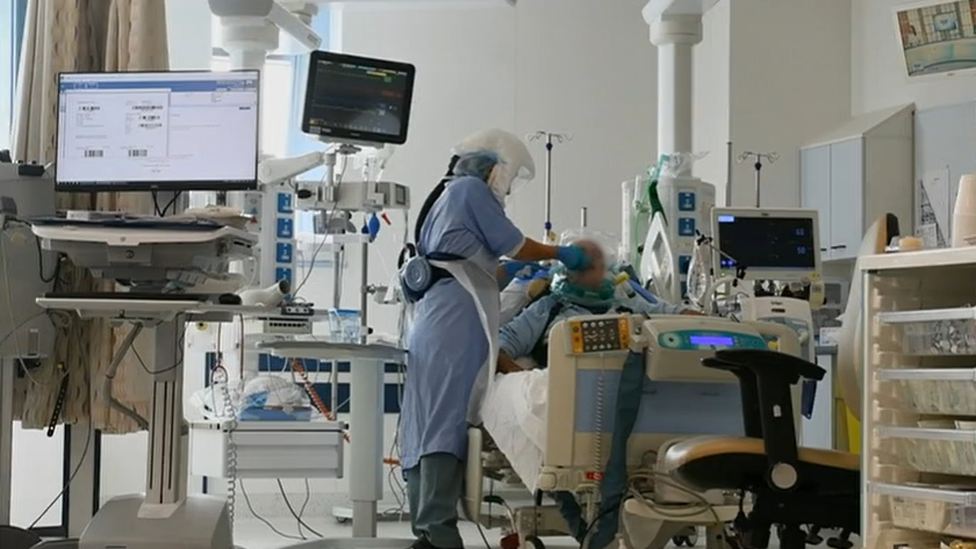 A patient (identity blurred and obscured) being treated in bed by a nurse in full protective gear at Glangwili hospital in Carmarthen during the height of the Covid pandemic.