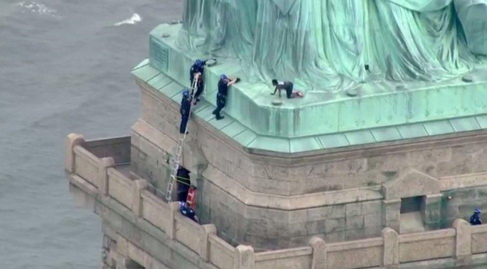 A screengrab shows police talking to a woman who climbed to the base of the Statue of Liberty in New York