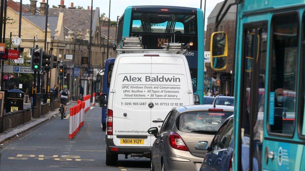 Traffic on Gosforth High Street, passing the row of bollards