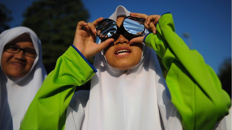 A girl in Malaysia looks at the sky through home-made glasses