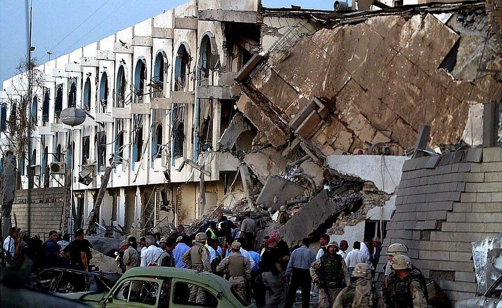 Injured and shaken UN workers are led away from the United Nations complex in Baghdad after a suicide bomb attack on 19 August 2003