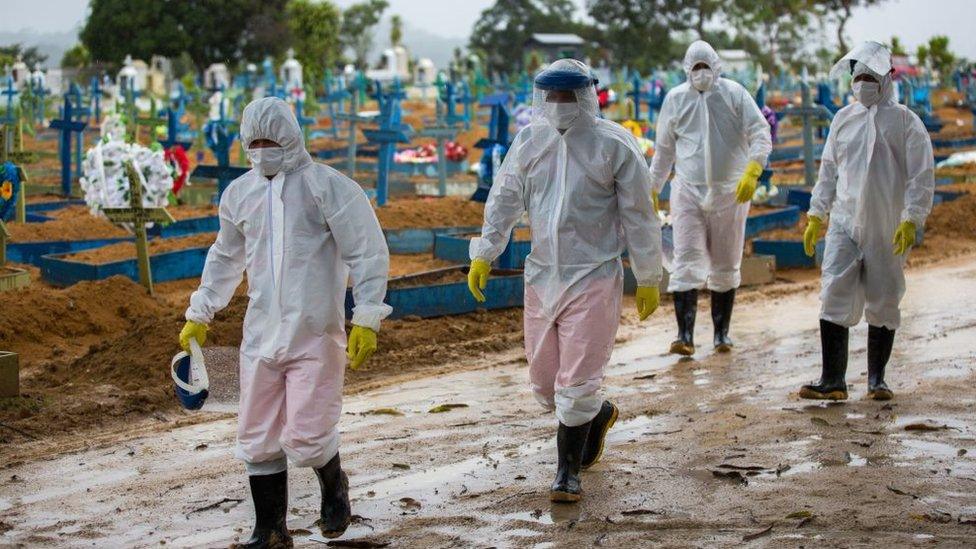 Workers wearing protective suits walk past the graves of COVID-19 victims at the Nossa Senhora Aparecida cemetery, in Manaus, Brazil, on 25 February 2021.