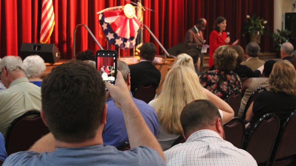 A man taking a photograph of Elaine Luria at the town hall event