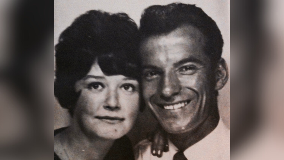 Carol and Raymond Lewis leaning their heads on each other. Both are smiling at the camera and the picture is in black and white.