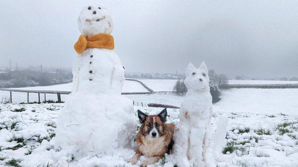 A snowman and snowdog alongside a real dog