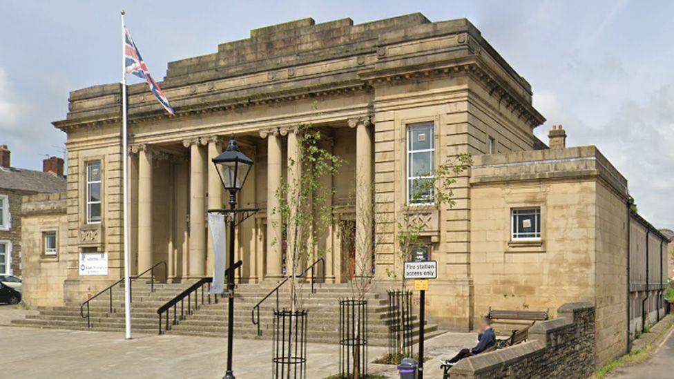 Mercer Hall is a large stone-built property with six large pillars at the entrance, above steps with black railings. It has a flagged frontage with a Union Jack flag flying from a flagpole and a vintage street lamp.