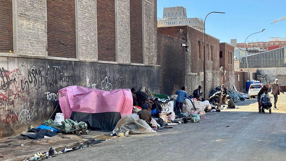 A row of makeshift tents and dwellings lie untidily on the roadside.