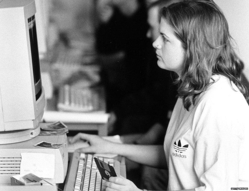 Woman on a computer, holding a floppy disk