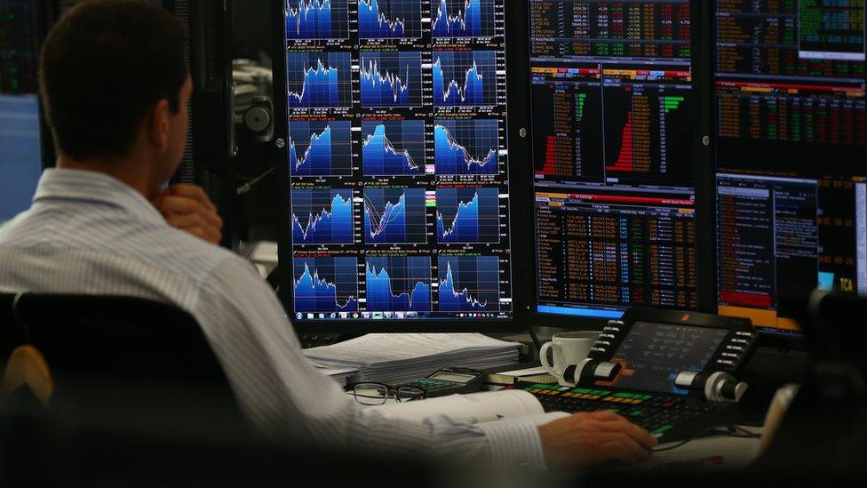 A currency trader in front of a series of screens showing currency prices