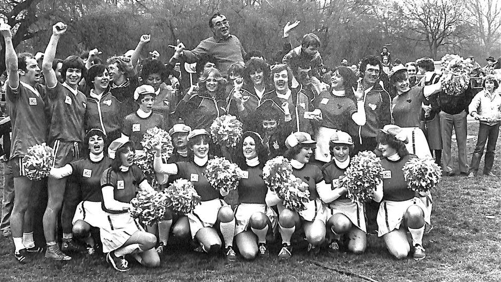 Black and white team photo with mainly women kneeling down and men standing up