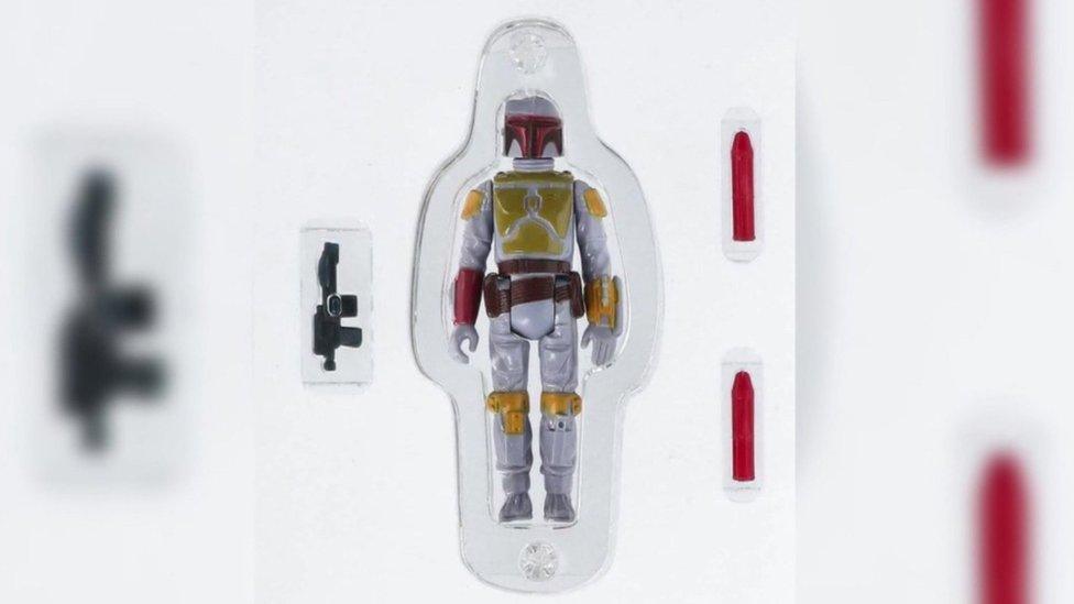 A picture of a Boba Fett Star Wars toy, still in its plastic casing - an armoured bounty hunter with weapons