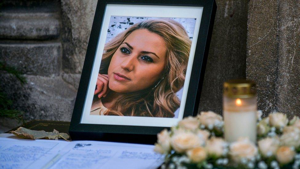 A photo frame showing a picture of Viktoria Marinova is seen laid against the stone walls of a church, with candles in tribute placed nearby