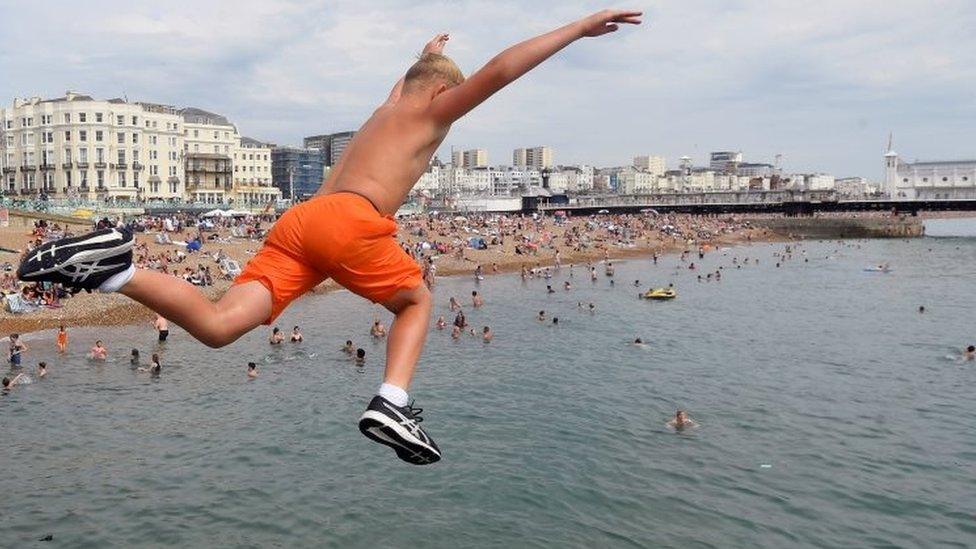 A boy jumps into the sea as he enjoys the hot weather at Brighton beach