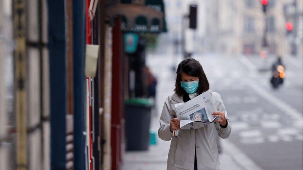 A woman wearing a protective face mask reads a newspaper as she walks in a street on the deserted Ile Saint Louis in Paris