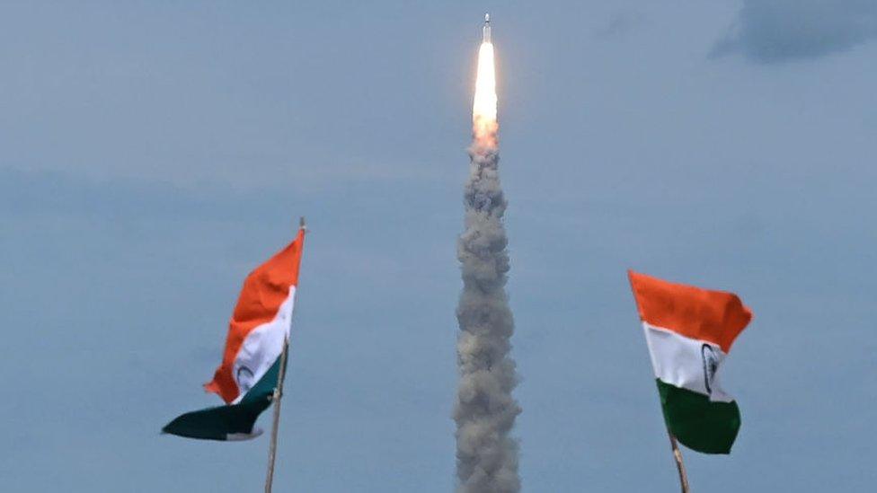 People wave Indian flags as an Indian Space Research Organisation (ISRO) rocket carrying the Chandrayaan-3 spacecraft lifts off from the Satish Dhawan Space Centre in Sriharikota, an island off the coast of southern Andhra Pradesh state on July 14, 2023. India launched a rocket on July 14 carrying an unmanned spacecraft to land on the Moon, its second attempt to do so as its cut-price space programme seeks to reach new heights. (Photo by R.Satish BABU / AFP) (Photo by R.SATISH BABU/AFP via Getty Images)