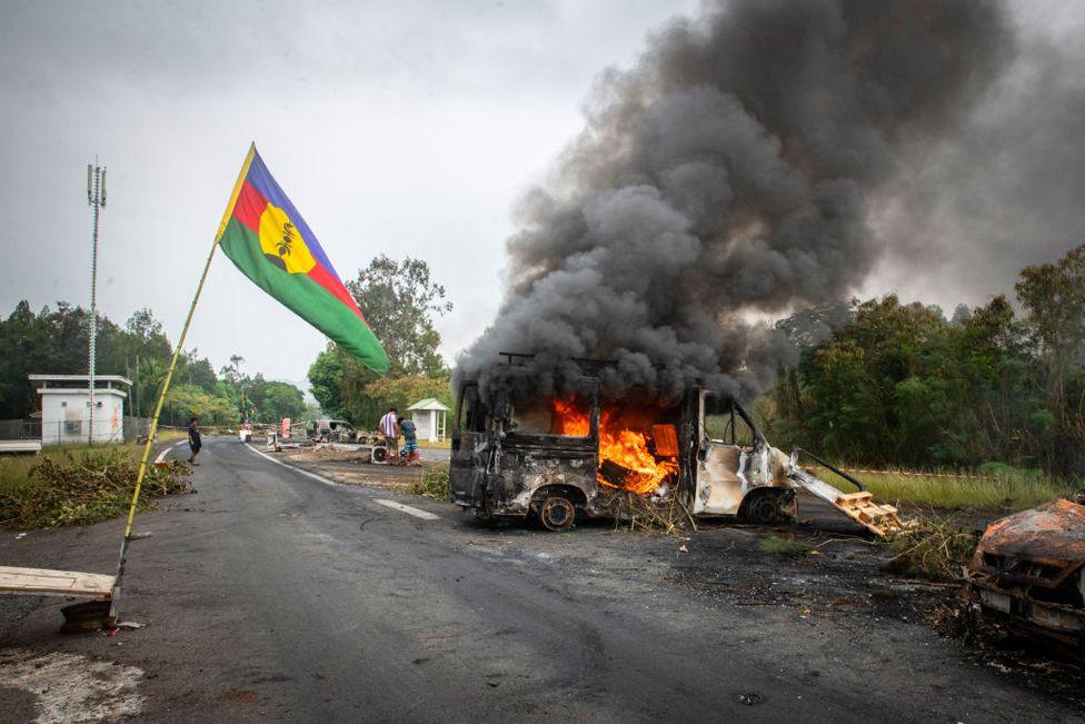 A Kanak flag waves next to a burning vehicle at an independantist roadblock at La Tamoa, in the commune of Paita, France's Pacific territory of New Caledonia on 19 May 2024