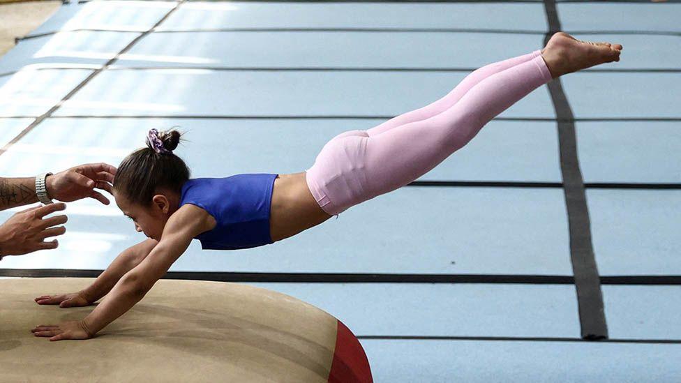 A generic image of a girl training on the vault during an artistic gymnastics training session, with her arms outstretched touching the vault and her legs raised together in the air