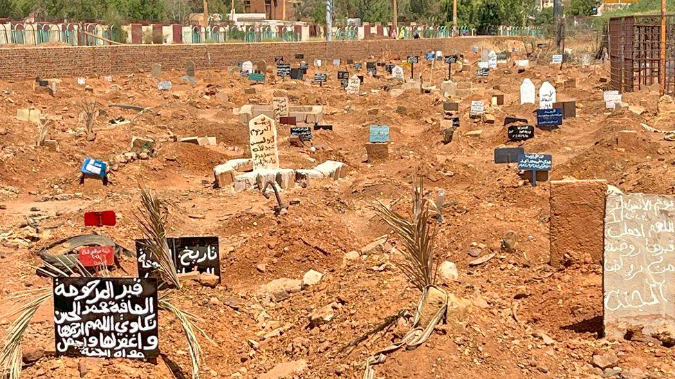 The Ahmed Sharfi Cemetery where mounds of orange bare earth can be seen, graves marked by makeshift signs or dead palm leaves