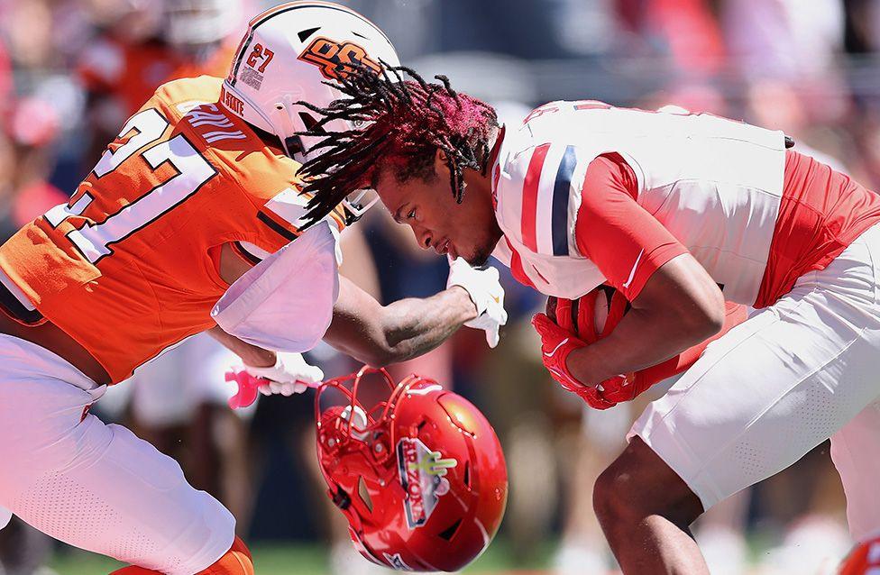 Arizona Wildcats’ Tre Spivey scores a 13-yard touchdown reception against the Oklahoma State Cowboys during the first half of an NCAA football game in Tucson, Arizona. The image shows a hard collision, with Spivey’s red helmet flying off as he secures the ball.