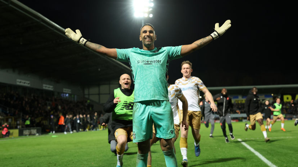 Goalkeeper Jasbir Sing in a green strip with his arms outstretched as team-mates run to celebrate with him