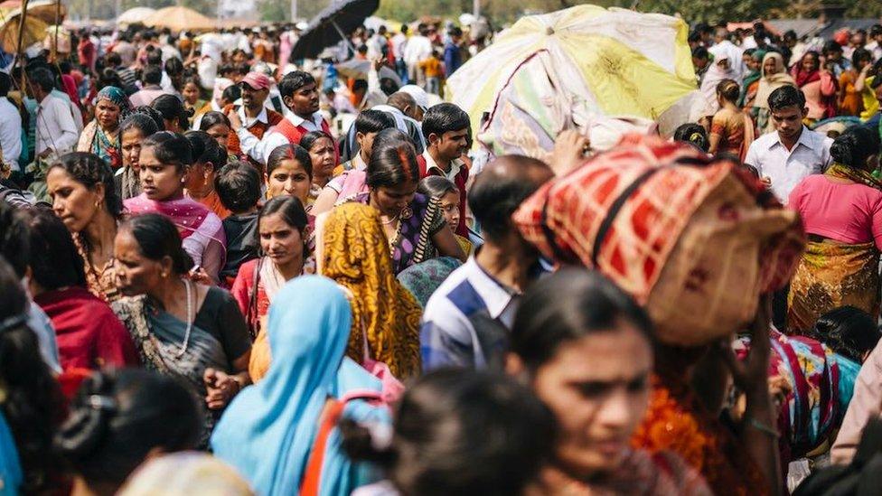 Men and women, some with umbrellas to shield from the sun in a crowded Delhi street