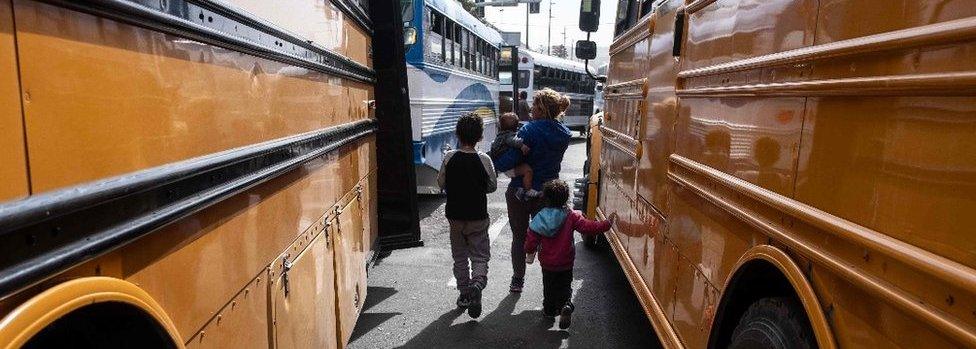 A Central American migrant woman and children walk next to buses in Tijuana, Mexico