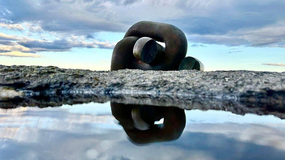 Two giant chain links on a rock reflected in a puddle