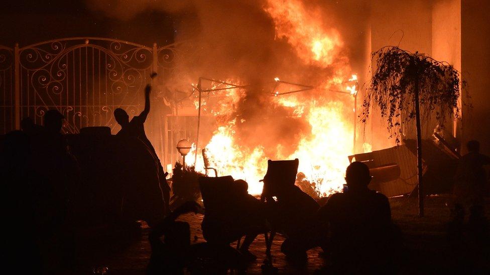 Fire dominated this image, raging in front of a tall ornate gate in the background, while in the foreground the silhouette of someone throwing an object can be seen outlines against the flames