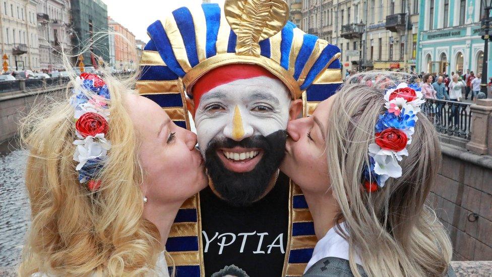 two Russian women kiss a fooball fan on the cheek