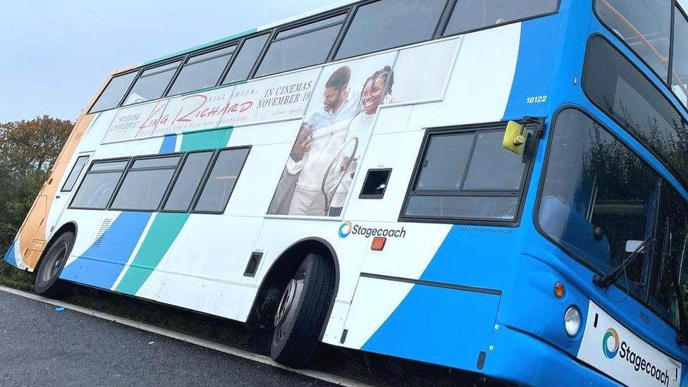 The bus leans onto a hedgerow