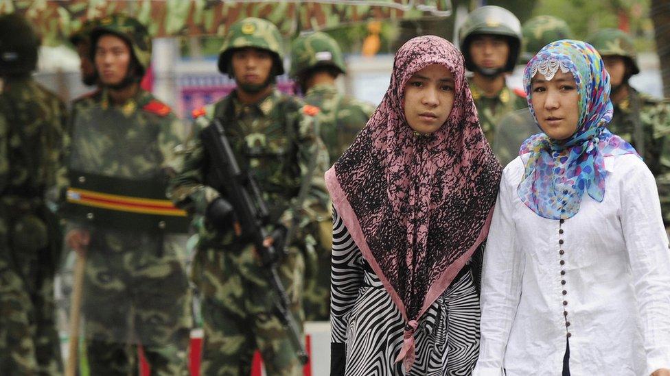 Two Uighur women pass Chinese paramilitary policemen in China's Xinjiang region