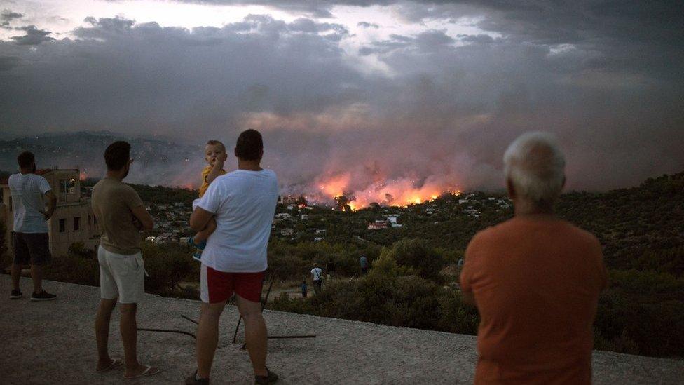 People watch a wildfire in the town of Rafina, near Athens