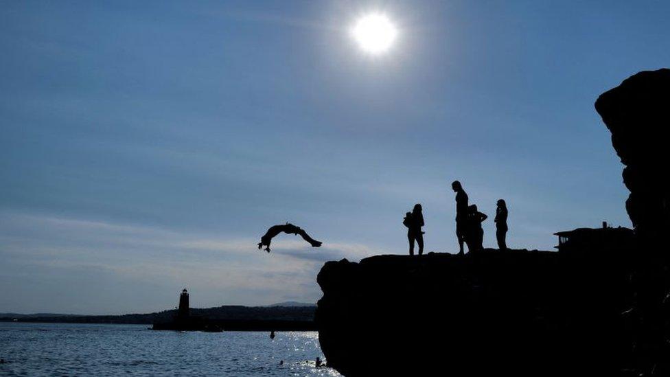 People jump from rock into the Mediterranean Sea in the French Riviera city of Nice, 10 July 2022