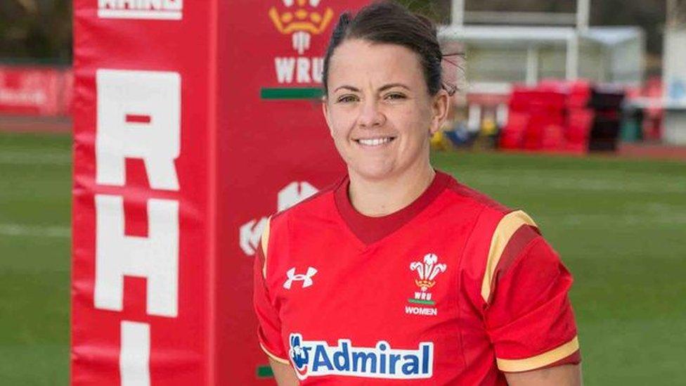 A photo of Sian Williams in Wales rugby gear, standing to attention by a padded goalpost on the field