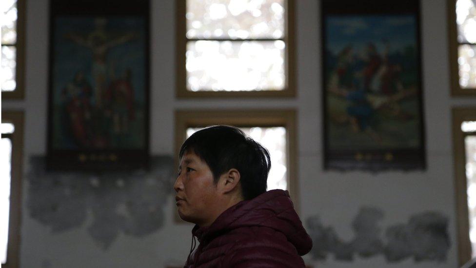 Someone in a quiet official church, with stained glass windows behind them.