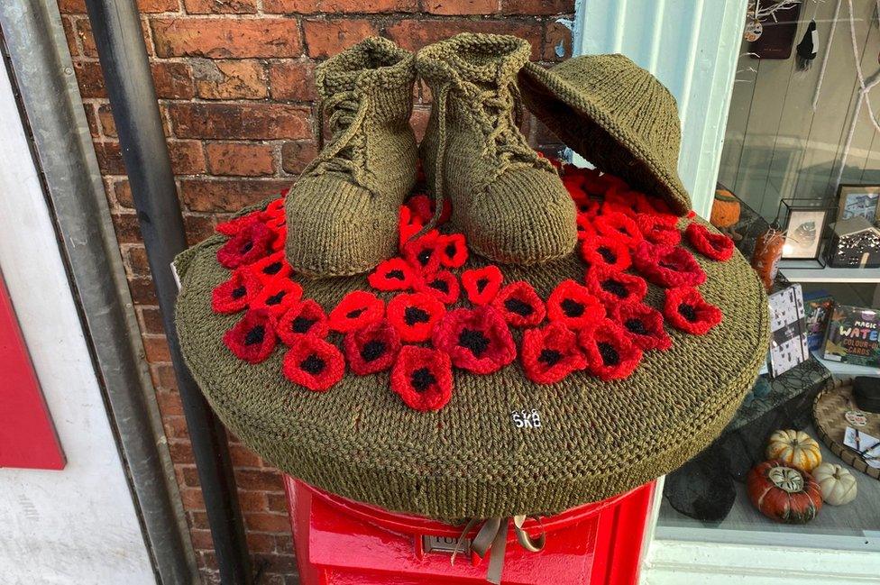 Knitted poppies, boots and helmet on a post box topper