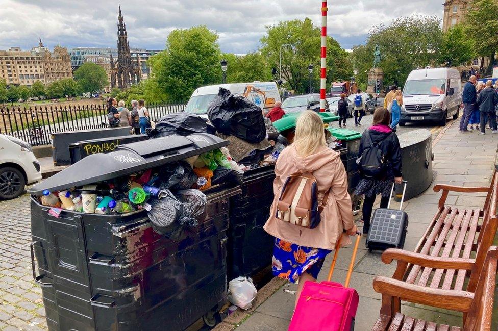 tourists walk pass overflowing bins