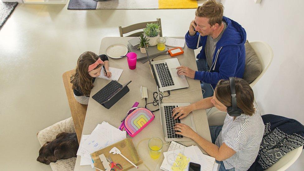 A family working from home sit around a dining table on laptops