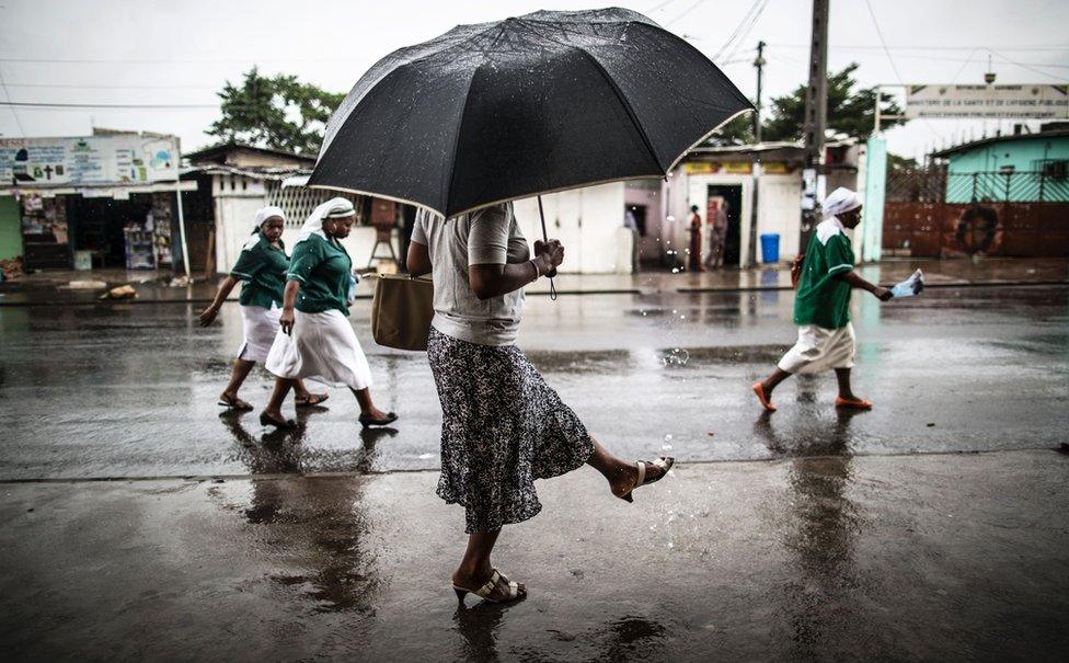 A woman washes a her foot with water streaming out of a pipe as catholic nuns leave the St. Michel Church in Libreville on 28 August 2016 after the Sunday's service