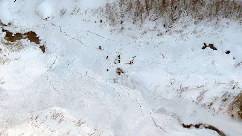 A distant group of rescue workers on skis can be seen in this top-down shot taken by helicopter