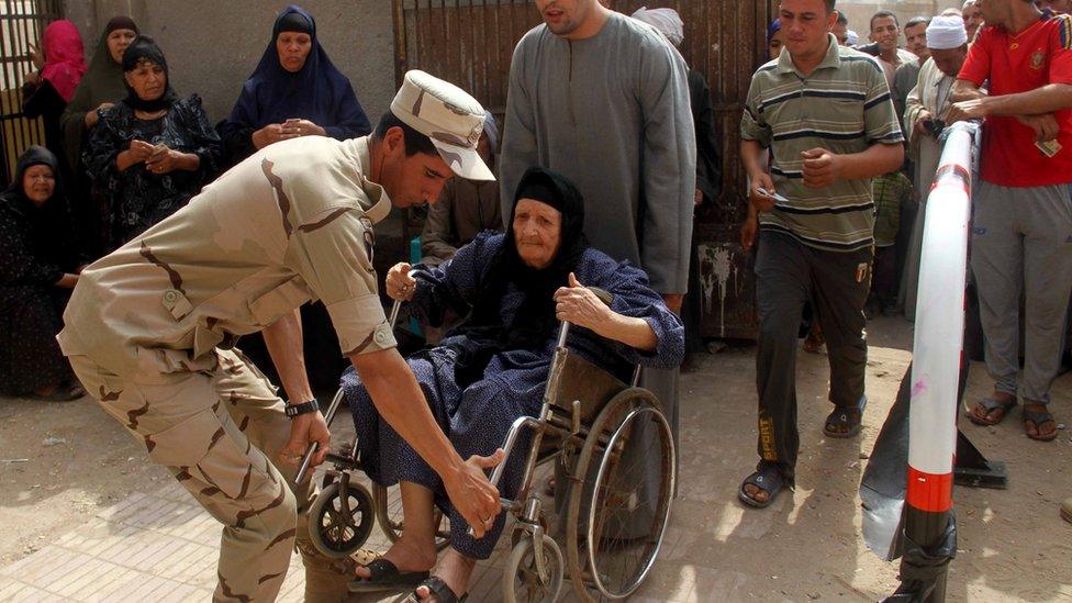 An Egyptian soldier and man help a disabled woman enter a polling station on the outskirts of Cairo's southern Giza district on 18 October.