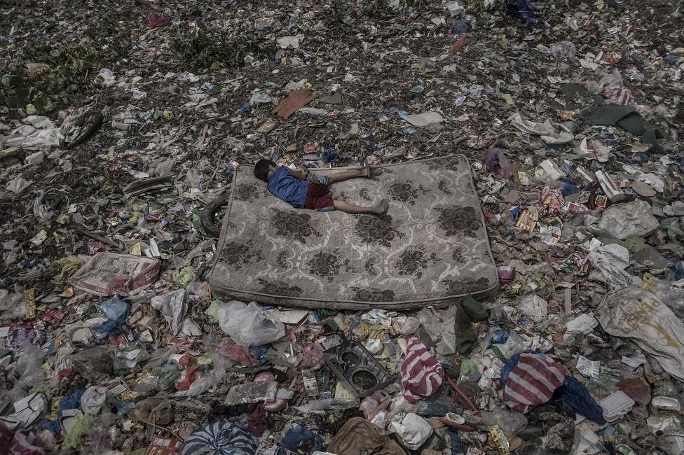 A boy lies on a mattress amongst rubbish