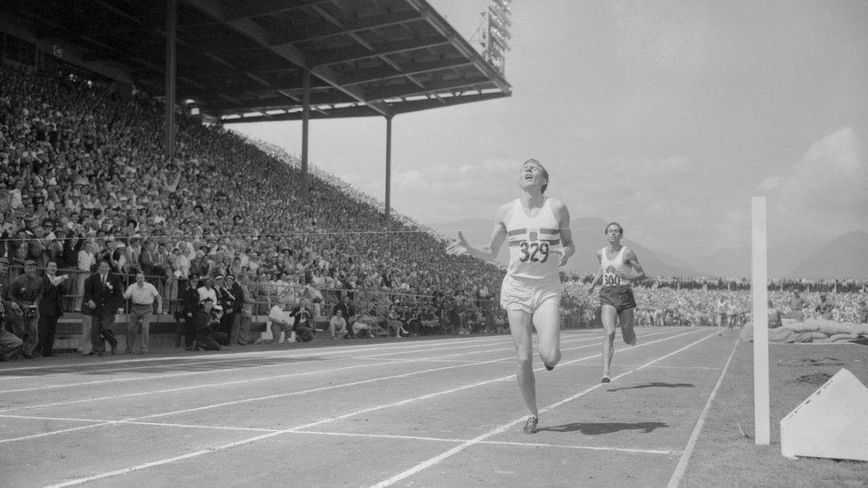 roger bannister crosses the finish line in a black and white archive photo with crowds watching and john landy looking on behind