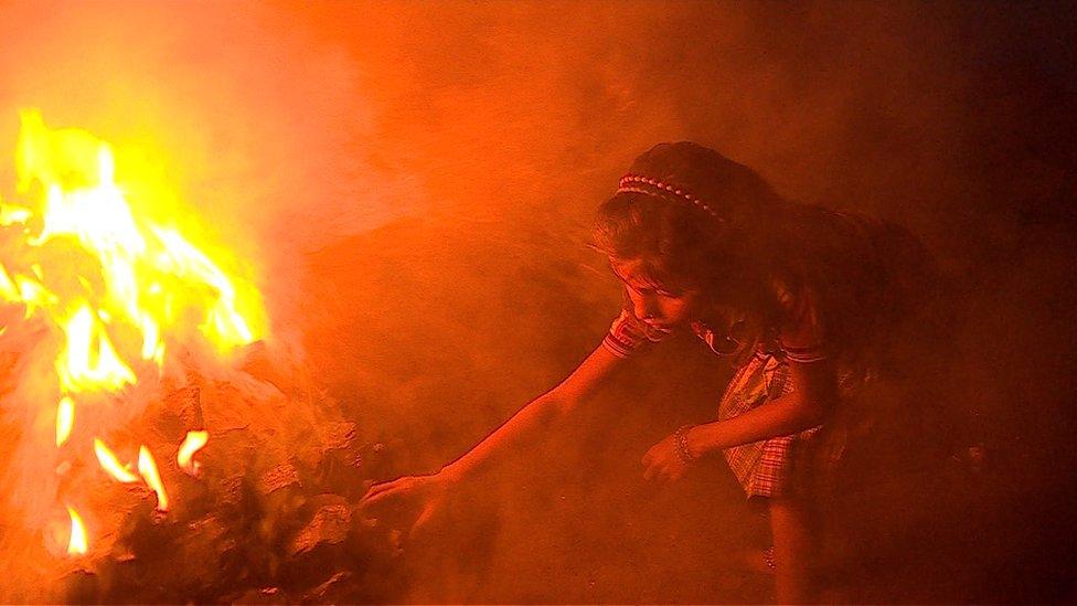 A young girl feeds a fire inside an open cast coal mine